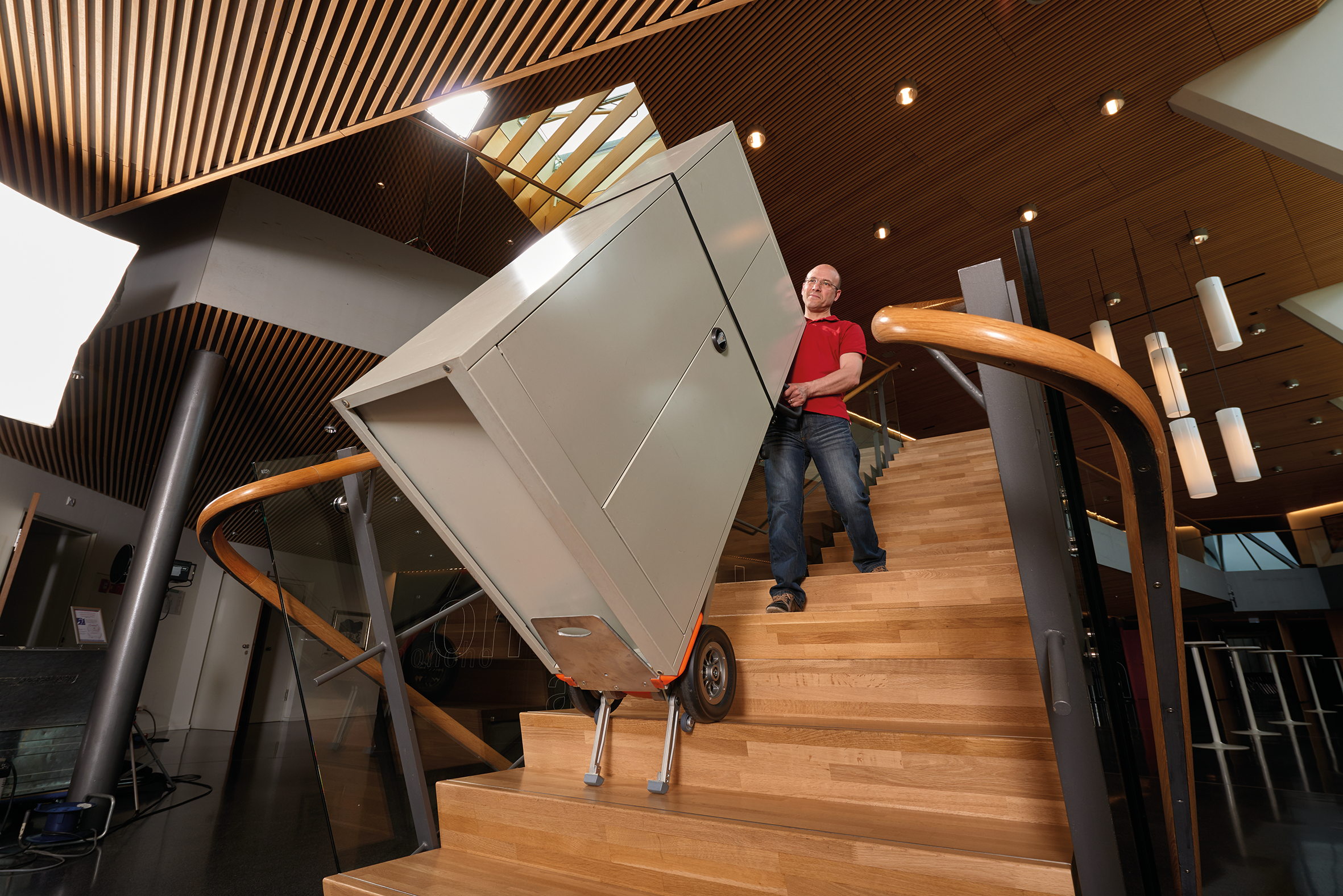 The picture shows a middle-aged woman using a CargoMaster stair climber for loads to carry five large green baskets of groceries up and down stairs at once. The woman looks very relaxed and hardly needs any strength. 