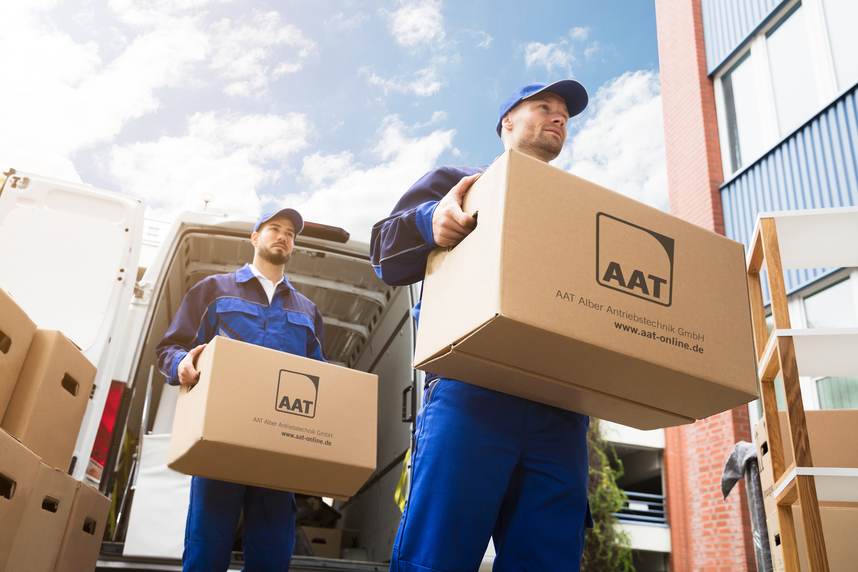 The picture shows two men from a delivery service transporting two large parcels. They do not look stressed. The picture is symbolic of smooth workflows without delays in processing.
