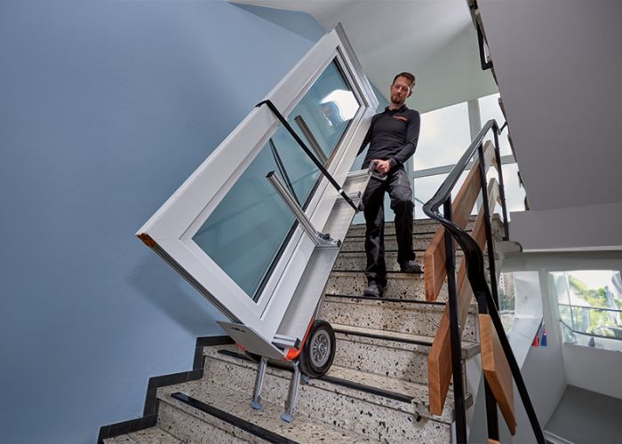 The picture shows the use of the CargoMaster stair climber with a special holder for doors and windows. It shows how a large glass door is transported up and down stairs.